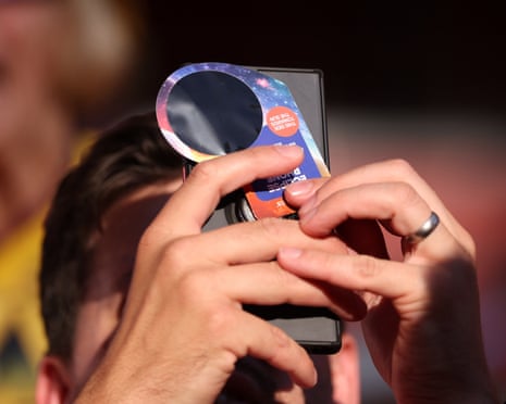 A fan of Arsenal puts a protective filter over their phone to watch the solar eclipse ahead of during the pre-season friendly match between Arsenal FC and Como 1907 at Emirates Stadium, London.