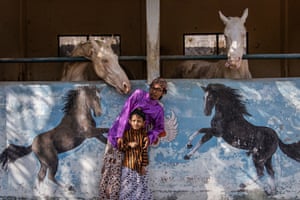 A man and a boy lean away as a horse in a stable tries to touch them with its nose