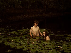 A young couple stand together amongst the lily pads in a pond.