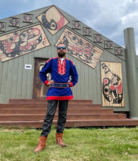 Andrei Zhvavyi, wearing traditional Sami clothing and standing in front of a wooden building decorated with traditional art