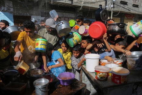 Palestinians crowd together holding empty plastic pots as they wait for food distribution in Rafah, southern Gaza Strip, on 8 November 2023. 