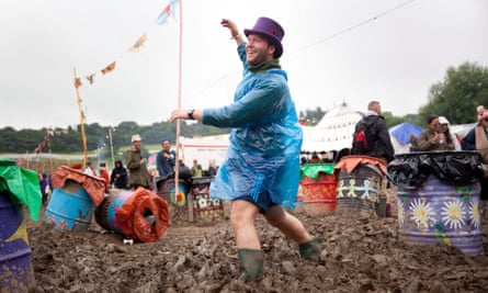 Man in a top hat and a plastic mac dances ankle-deep in mud at Glastonbury 2016