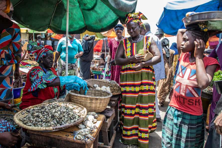 Muitas mulheres em vestidos coloridos em um mercado. Uma mulher em uma barraca com luvas de borracha mede ostras de uma cesta