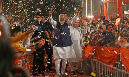 Prime Minister Narendra Modi holds his arms above his head flashing the victory sign among a crowd as confetti falls around him.