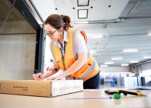 Sara Van Cotthem wearing an orange hi-vis vest leaning over a cardboard box.