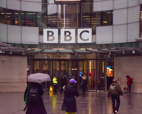 people in front of BBC headquarters holding umbrellas in the rain