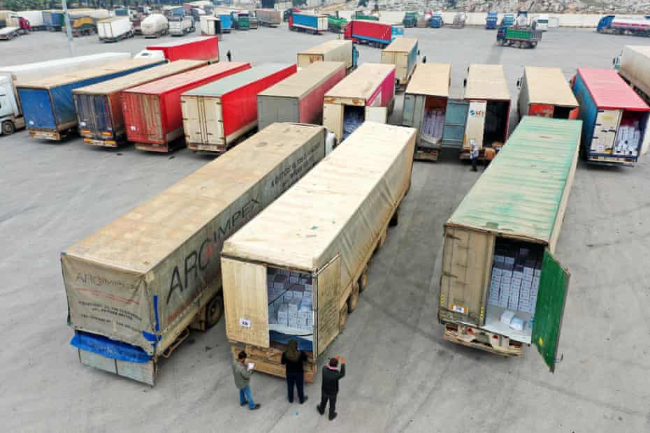 At least a dozen lorry trailers are lined up in the photo. Trailers in foreground have rear doors open, showing boxes stacked