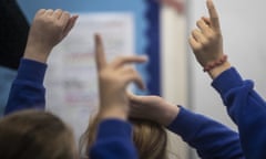 Back of heads of a couple of school children in a classroom with hands raised