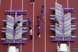 An athletics track with dismantled hurdles organised into two rows, attached to buggies, with people organising them