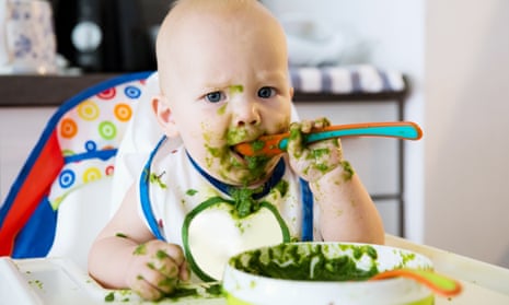 baby feeding - a very messy baby eating green mush in high chair.