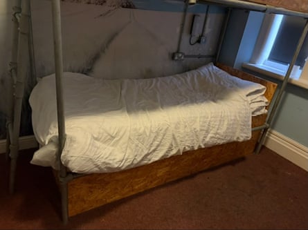 A bottom bunk of a bed is seen with dirt and mould on the wall behind it.