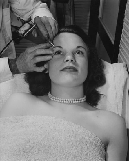 A tattoo artist tattooing a woman’s eyebrows, London, circa 1930