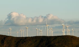 wind turbines on a hill against puffs of clouds in a blue sky