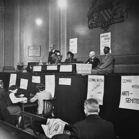 Black-and-white image of people looking up at a panel of speakers on stage