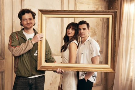 Shanks holds a large empty picture frame, behind which they stand, framed by it
