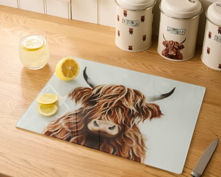 A chopping board with an image of a highland cow on a kitchen worktop with sliced lemons and a glass with lemonade and two lemon slices