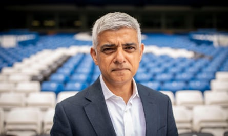 Sadiq Khan seen at Chelsea Football Club, 8 August 2024: a head and shoulders portrait as he stands in front of lines of blue and white seats
