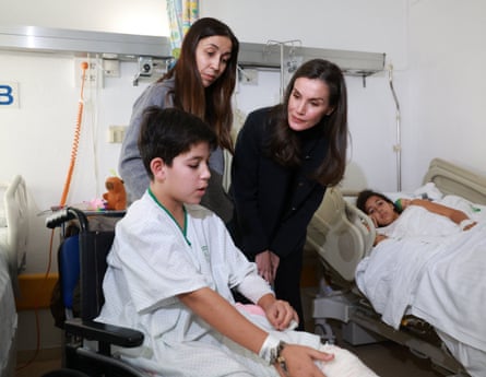 Queen Letizia leans over to speak to young boy.