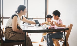 Mother teaching how to make paper crafts to her kids while working with laptop in the living room.
