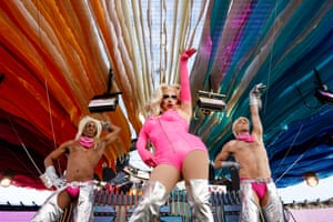 A drag queen in a pink bodysuit with two dancers