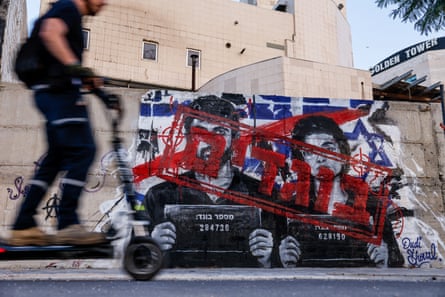 A man rides a scooter past graffiti depicting Yuval Abraham and Rachel Szor, with the word ‘traitors’ in Hebrew, on a wall in Ashdod, southern Israel.