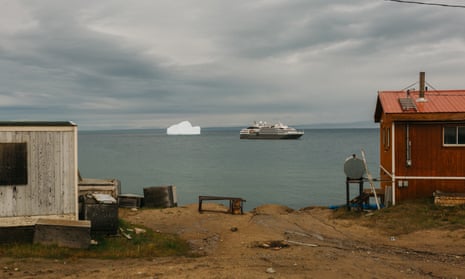 Cruise ship next to iceberg with two cabins on land in foreground