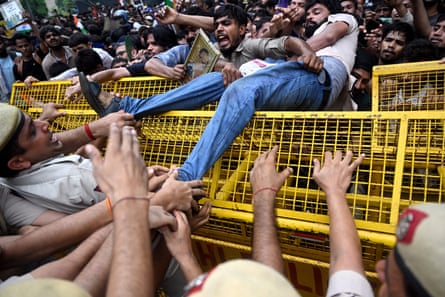 Police grab at the legs of a young man who is half over a metal barricade