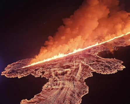 Smoke and fire rises into the darkened sky as lava flows during a volcanic eruption on the Reykjanes peninsula
