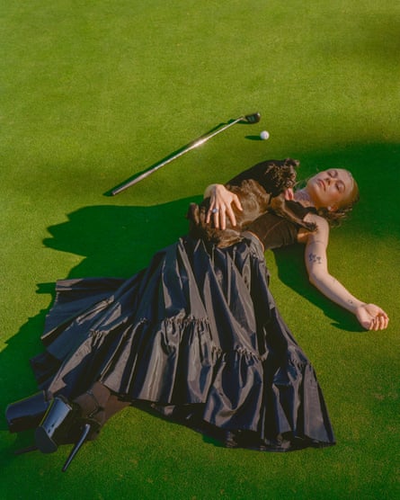 Phoebe Bridgers lying on a golf course wearing a vintage outfit and with a pug