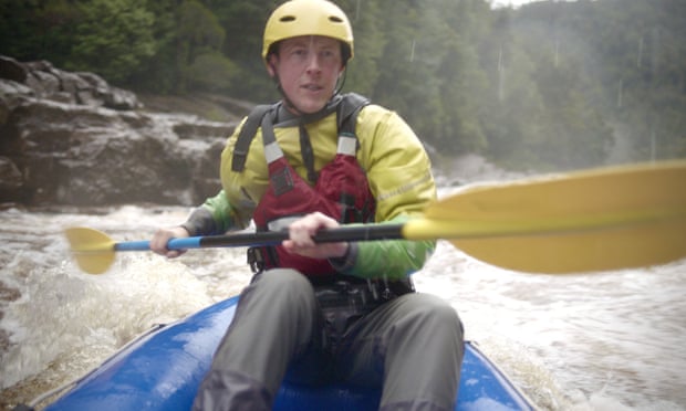 Oliver Cassidy rafting on the Franklin River. Cassidy is padding his blue raft through some rapids. He is wearing a life vest and helmet