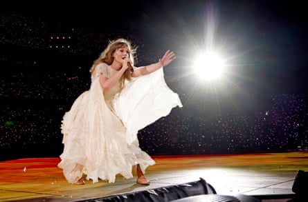 Taylor Swift gestures while singing in a long flowy white gown