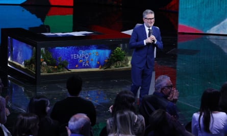 Fabio Fazio stands with a microphone in front of an audience in a TV studio