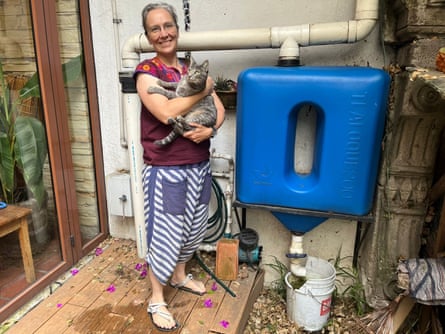 A woman holding a cat stands beside a blue plastic tank, part of a 5,000-litre rainwater-harvesting system.