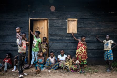 Young men, women and children outside a wooden hut