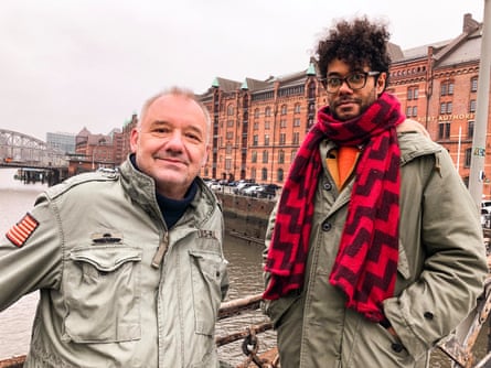 Bob Mortimer and Richard Ayoade standing on a bridge wearing green anoraks