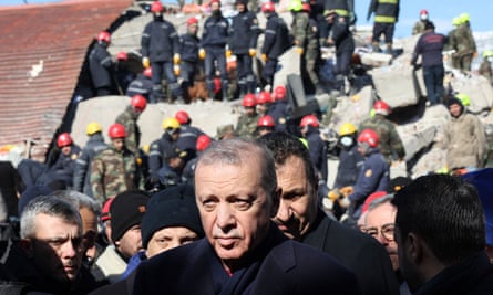 Turkey’s Erdoğan in front of a destroyed building and surrounded by people 