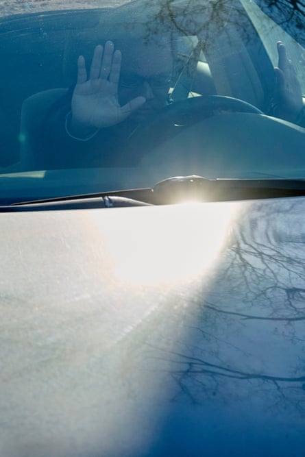A man raising his hands in a car, a tree reflecting on the car hood