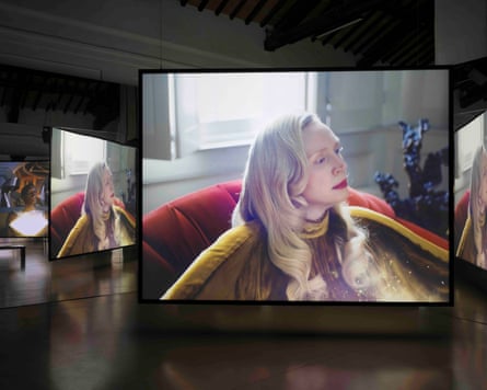 An installation featuring two screens of a film by Issac Julien starring Gwendoline Christie (pictured) sitting in a red chair wearing her long blond hair down.
