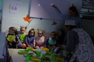 Children wait to be served food in a dimly lit bomb shelter