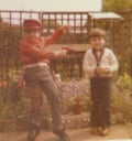 Two boys, one wearing a red hat and top, pointing a red toy gun at the other