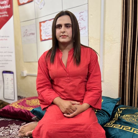 A woman dressed in red sits indoors on cushions on the floor