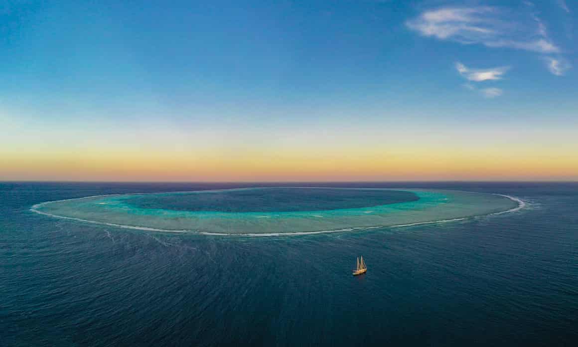 Aerial view of a circular reef, distinguishable by its light blue and brown colour, in the sea