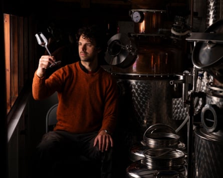 A man looking at a glass next to a brewing still