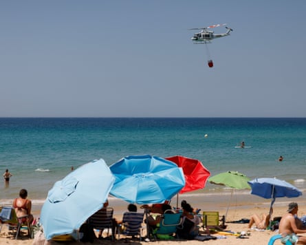 ‘Truly unprecedented’ … a firefighting helicopter collects water near Atlanterra Beach, Spain,