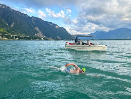 Neil Gilson swimming in a lake on a bright day with a support boat nearby