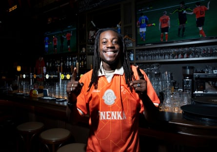 man in an orange football top standing in front of the bar