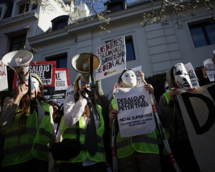 Protesters are holding megaphones and signs and wearing white masks