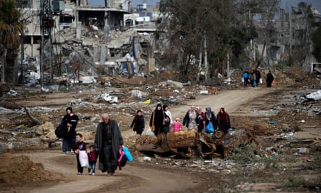 Men, women and children walking through landscape of destroyed buildings