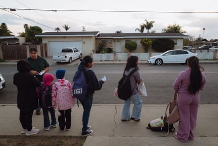 Vasquez in a green shirt distributes flyers to a row of parents and children