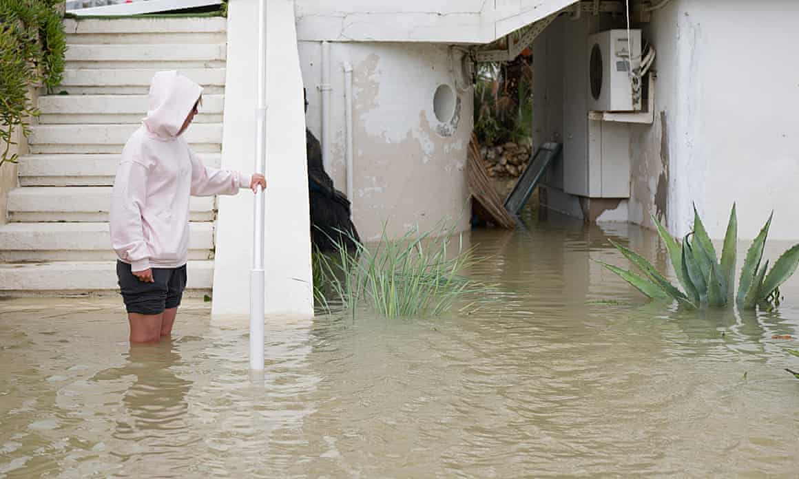 A person standing knee-high in water on a flooded street.